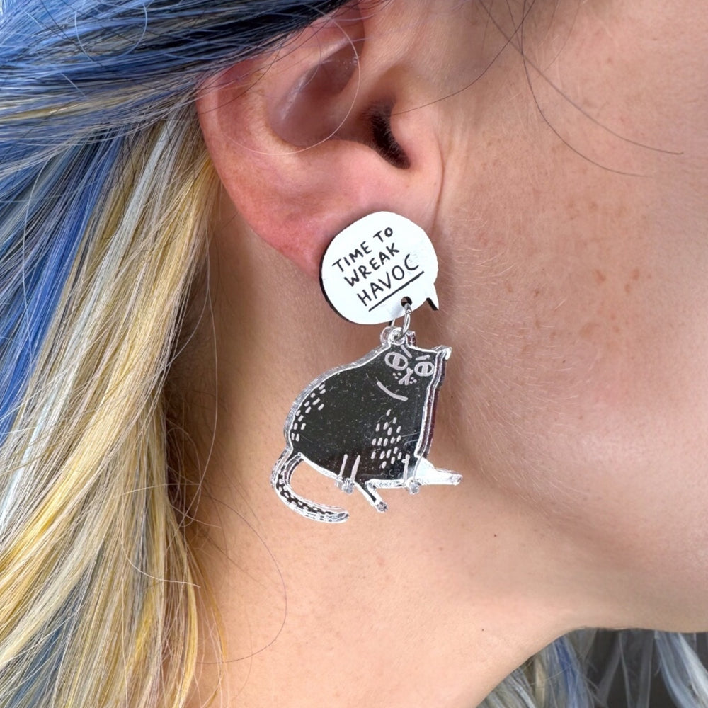 Earring with a cat design and 'Time to wreak havoc' text worn by a person with blue hair.