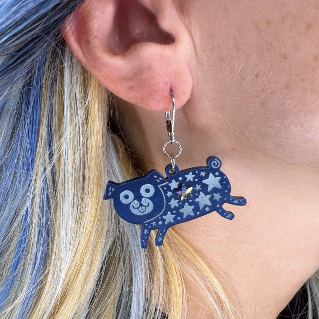 Creature of the Night pug dangle earrings with star pattern in pearlescent blue is worn by a person with blue hair.