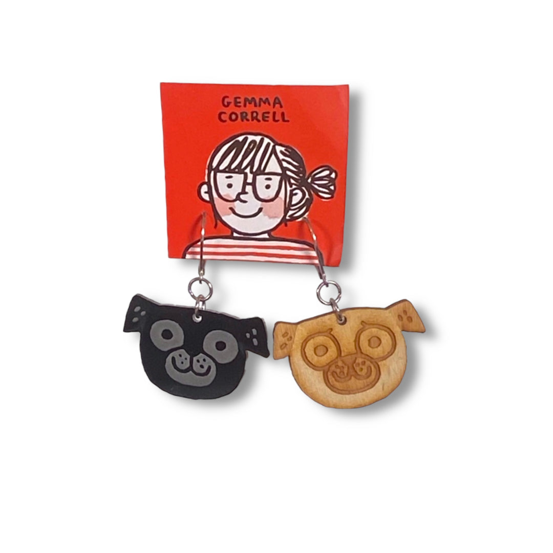 Asymmetrical pug dangle earrings on a red Gemma Correll branded card set against a white background.
