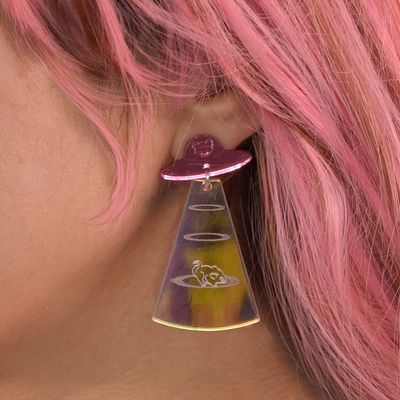 A woman with bright pink hair wears a pink and iridescent Cat from Meow-ter space earring. 