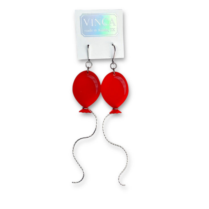 Our Red Balloon Dangle Earrings are seen on a white branded Vinca card and float against a white background.