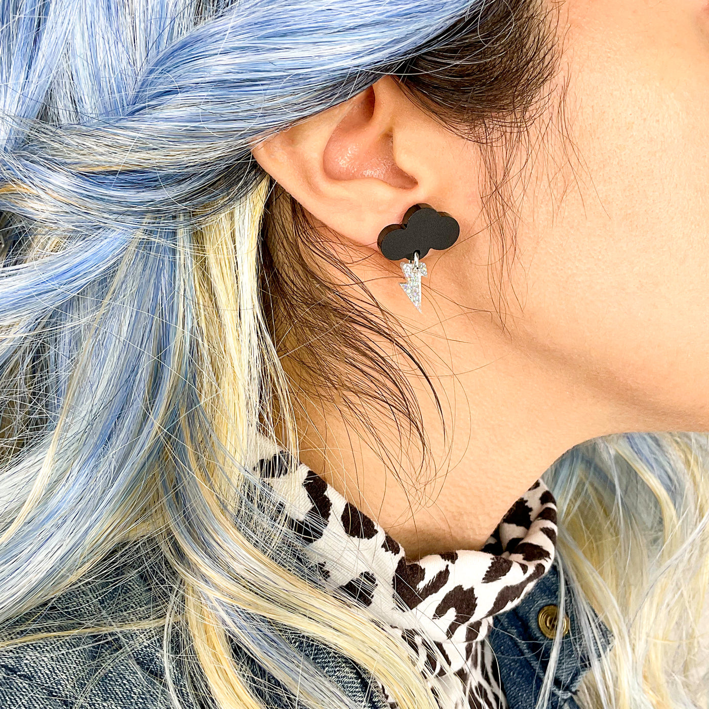 Matte black baby cloud earrings with hologram glitter bolt on an alternative styled woman with blue hair.
