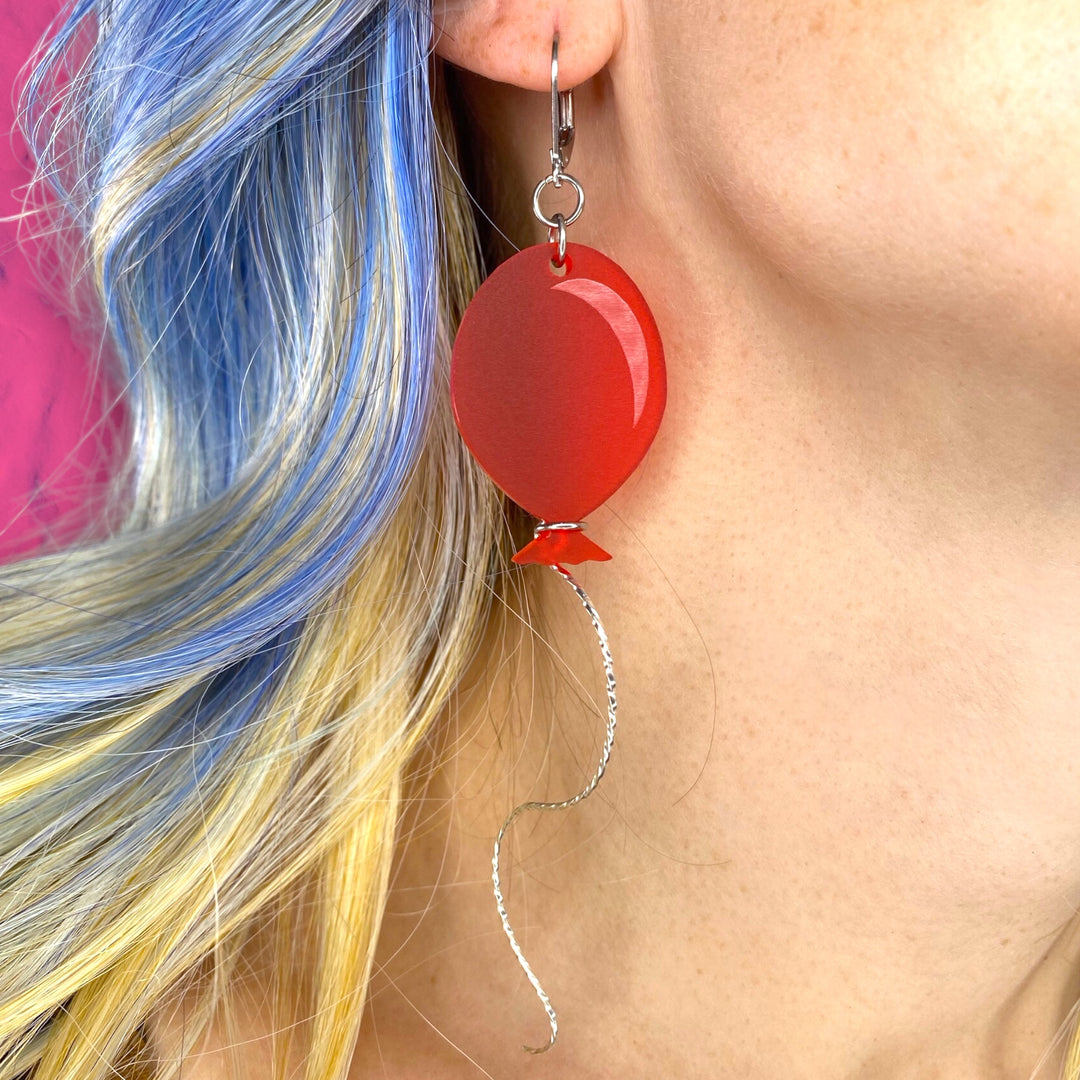 Our Frosted Red Balloon Dangle Earrings are worn by a model for scale.
