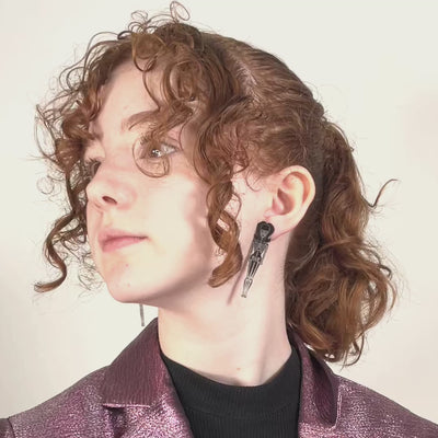 A young model with curly red hair wears skeleton doll earrings that glow-in-the-dark.
