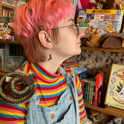 A young woman with short pink gradient hair wears a vampire bat ear threader earring in a toy store.