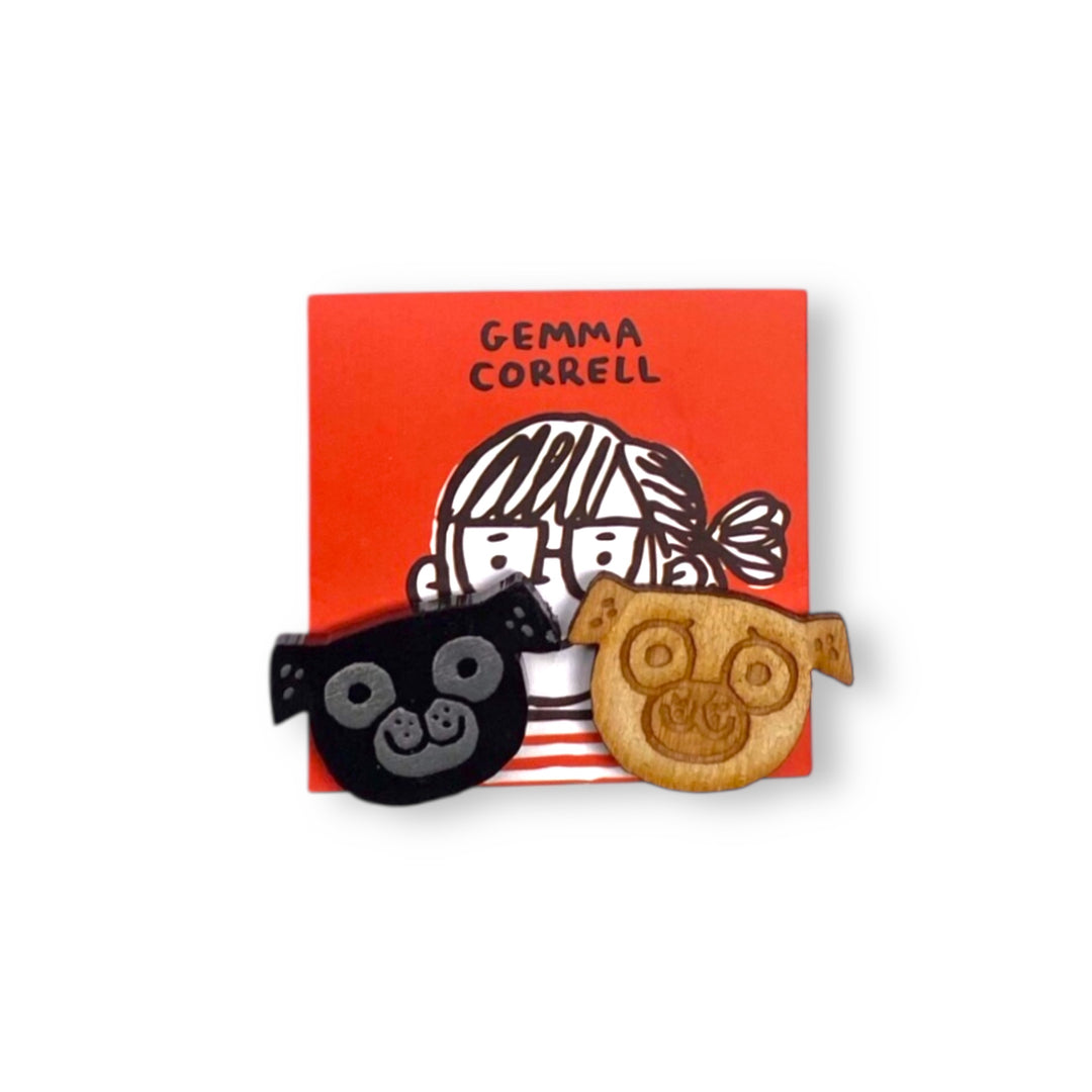 An asymmetrical pair of pug dog stud earrings on a red  Gemma Correll branded card set on a white background.