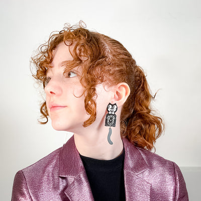 Young model with red curly hair wears an officially licensed, extra large Kit-Cat Klock earring in white and black.