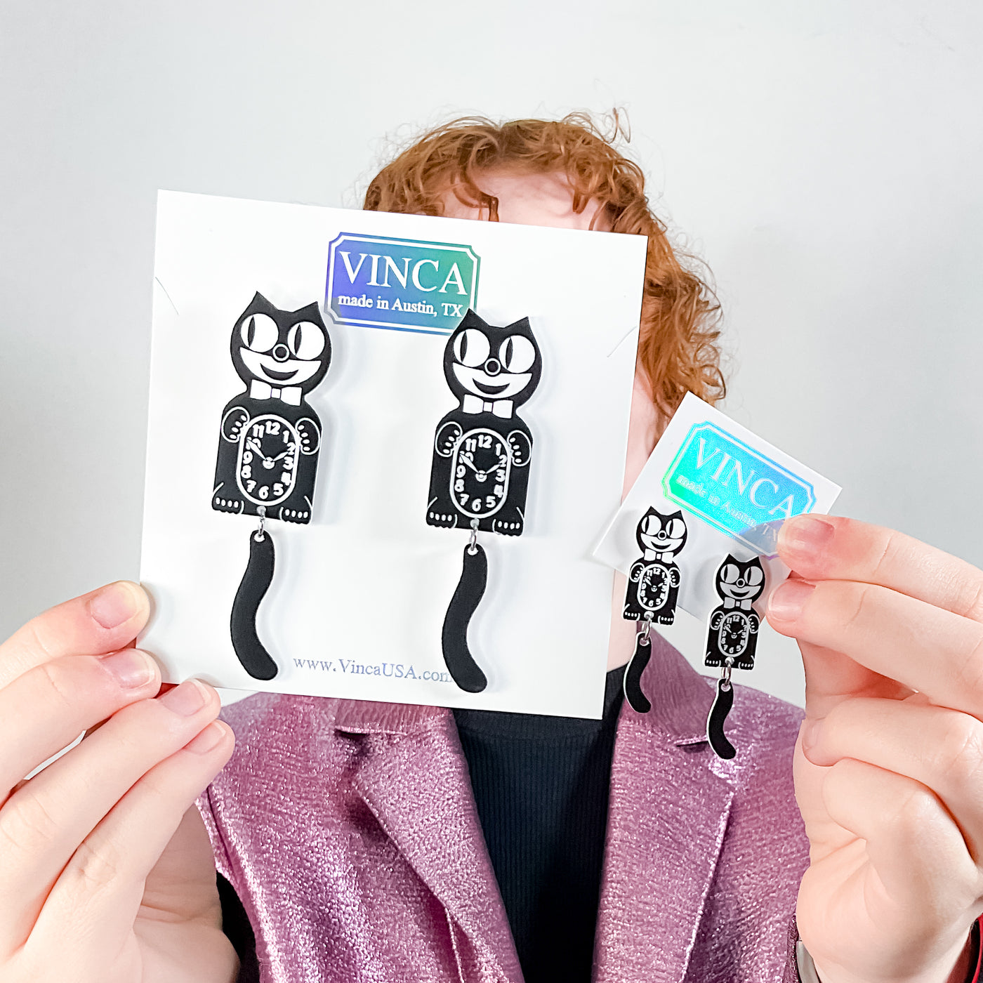 Extra large Kit-Cat Klock earrings versus small earrings held up by a young model with curly red hair.
