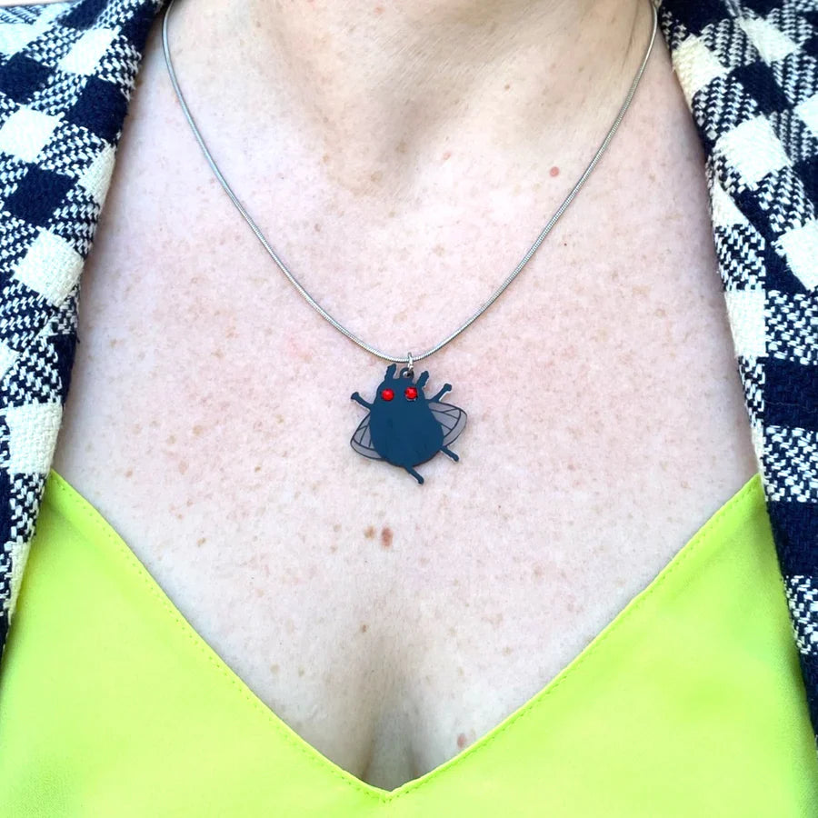 A woman with a flannel blazer and neon green shirt wears a Sarah's Scribbles designed moth man necklace.