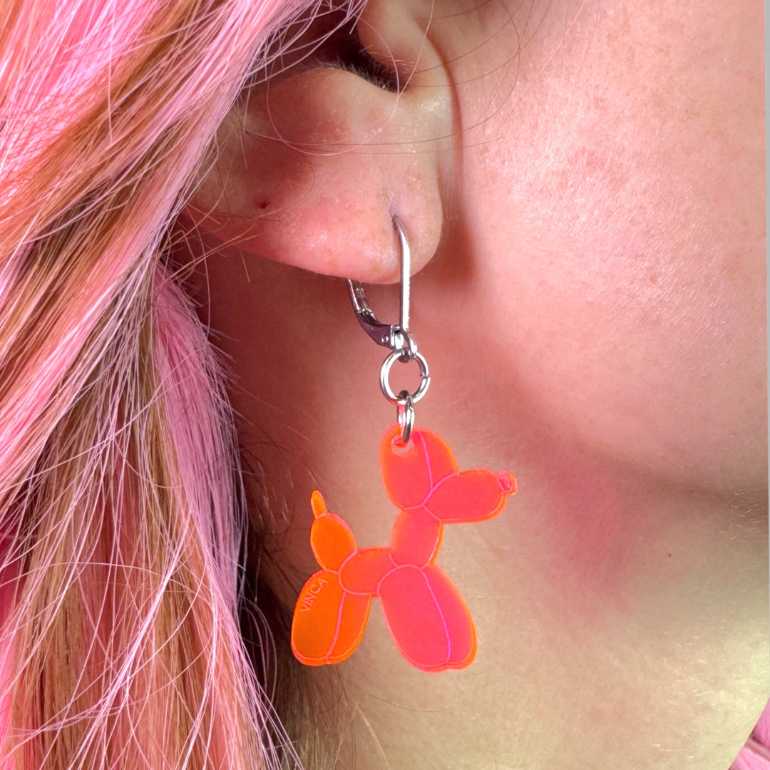 A woman with bright pink hair wears a transparent neon pink Balloon Dog dangle earring. 