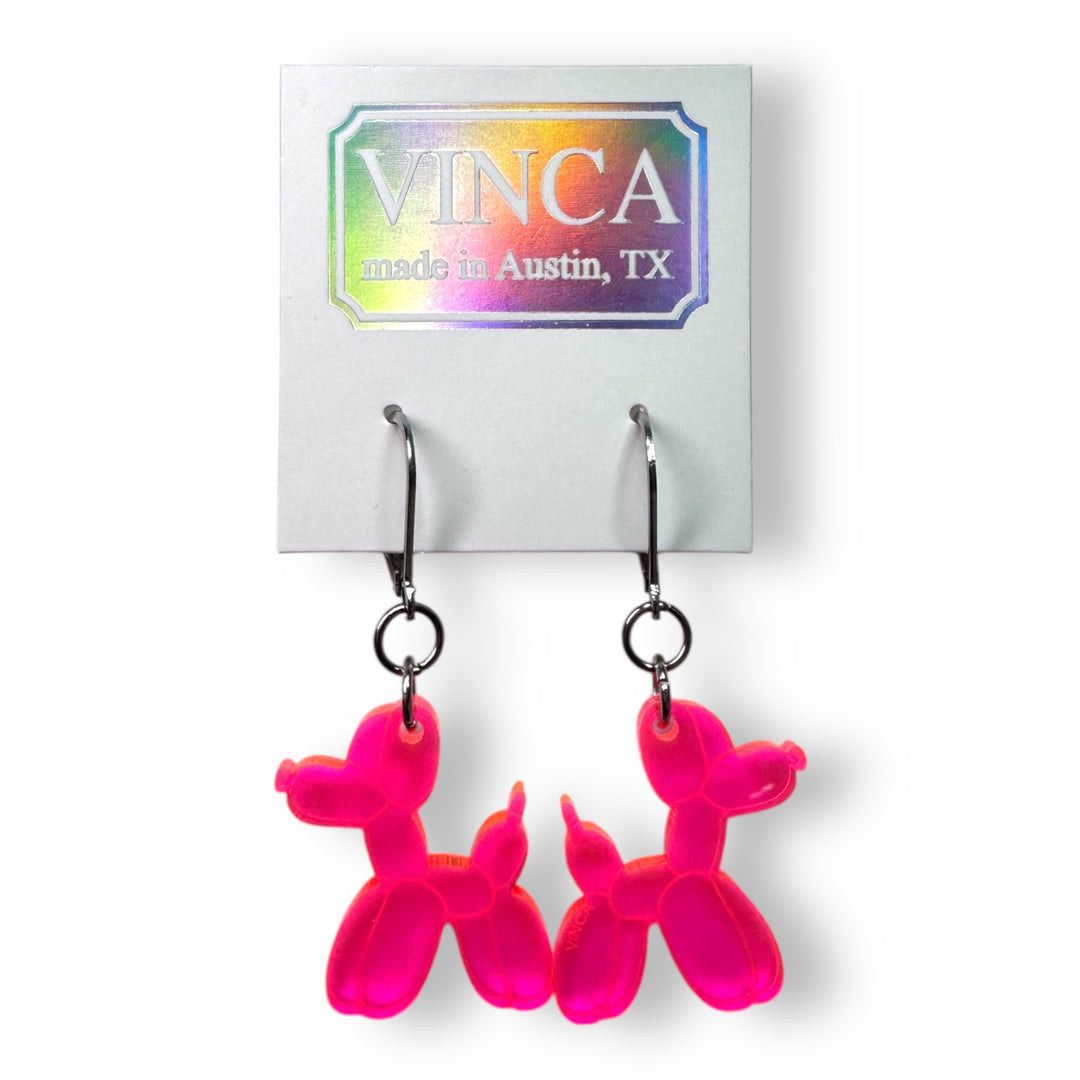 handmade Balloon Dog Dangle Earrings in transparent neon pink are attached to a white branded card. 