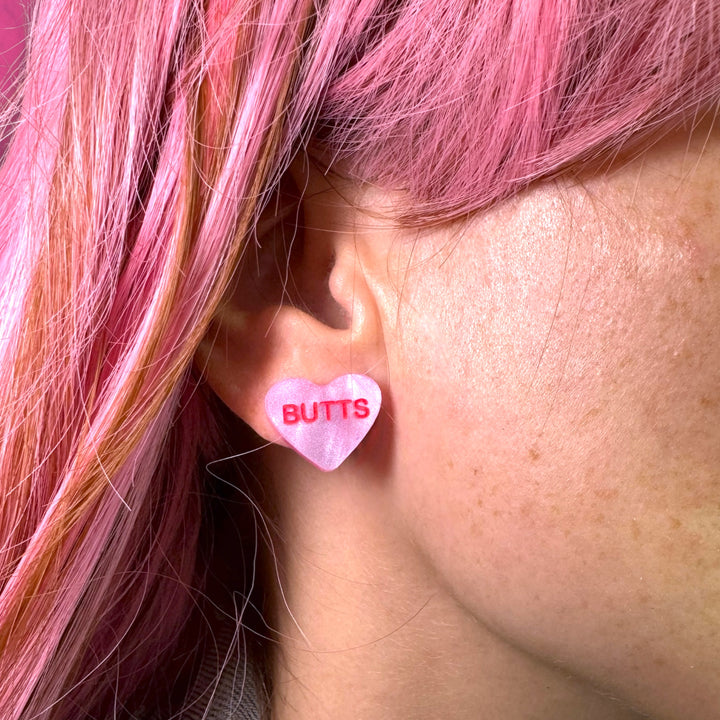 Butts Valentine's Day conversation candy heart earring in pearl pink on a model with pink hair. 