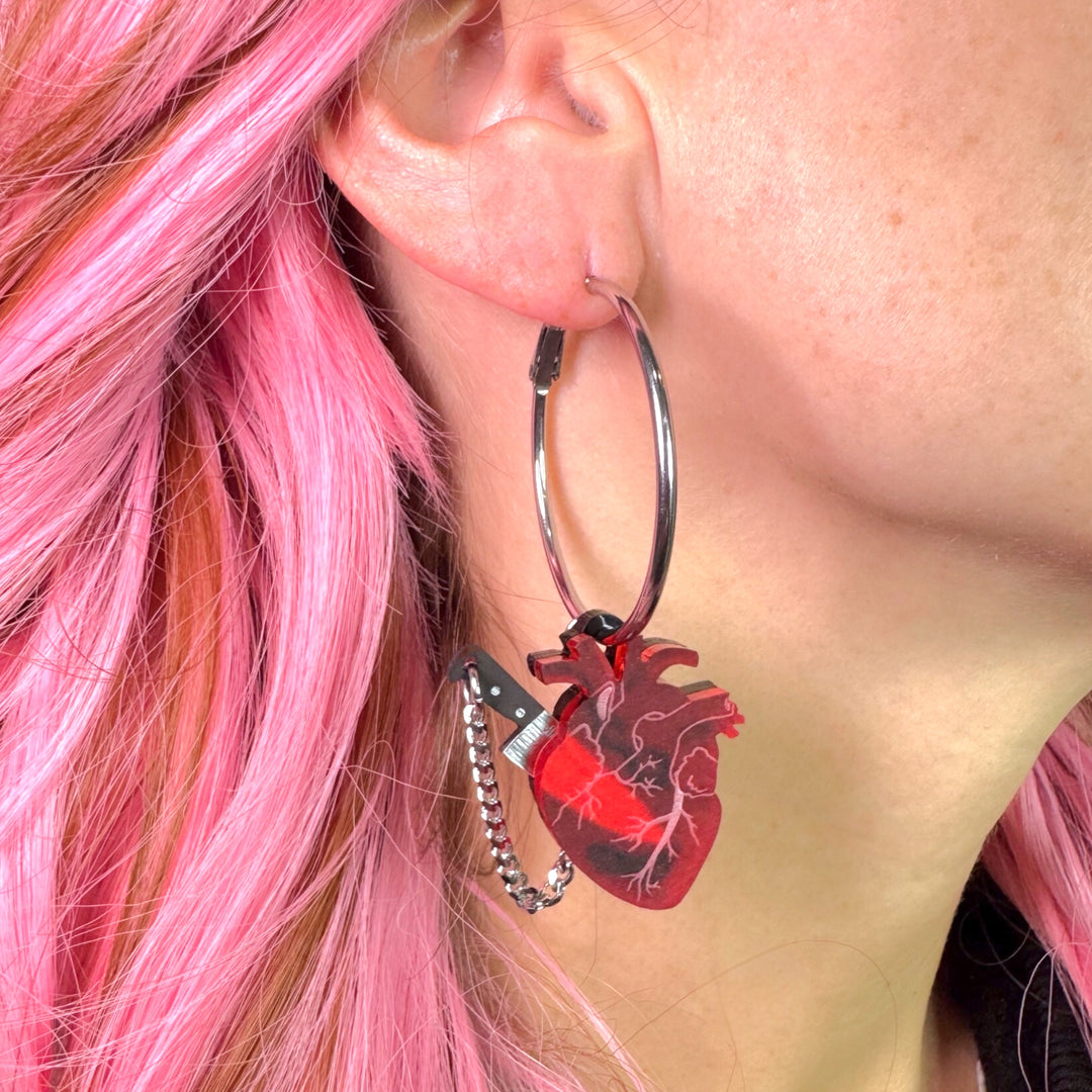 This is the original Chopped Heart Hoop earring design.
Chopped anatomical heart hoops with stainless steel hoops and frosted red anatomical heart charm with silver tone knife. Yes, the knife is removable!