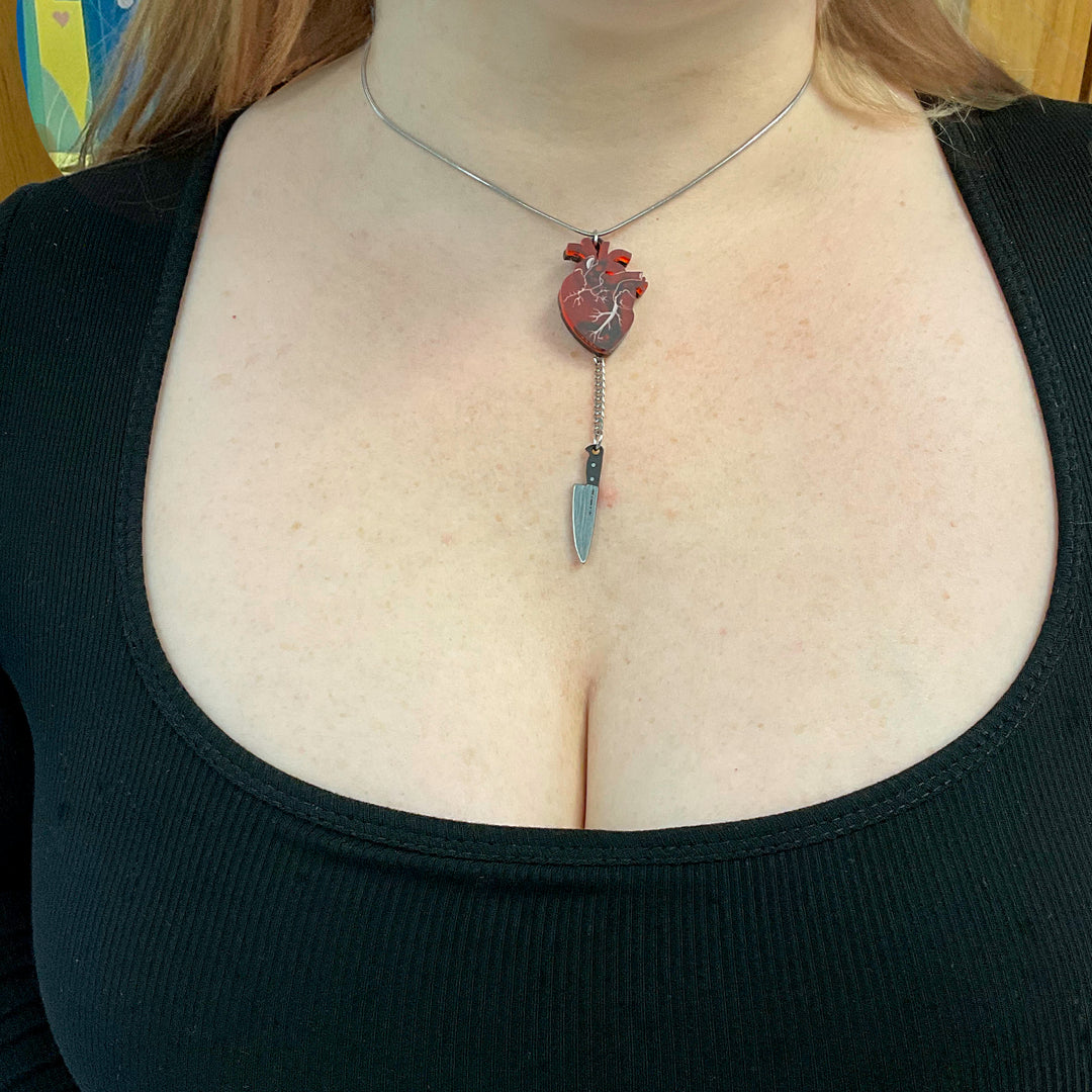 Chopped anatomical heart necklace in frosted red and stainless steel with plastic silver tone knife.