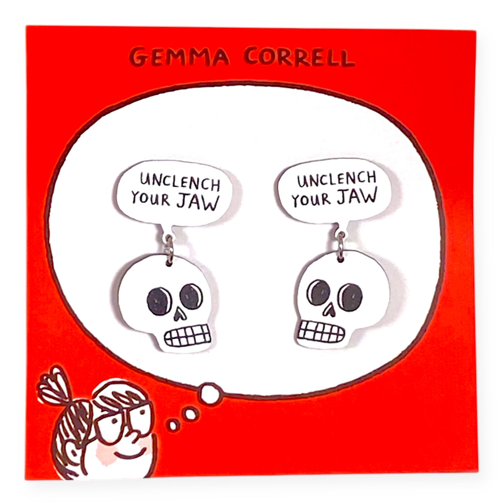 Skull-shaped earrings with 'Unclench Your Jaw' speech bubble on a red card with 'Gemma Correll' branding.