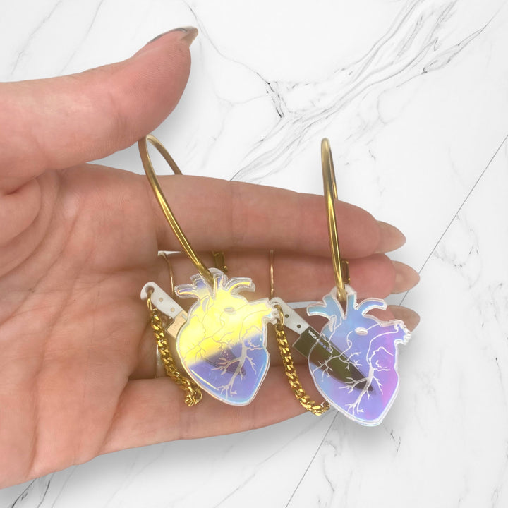 Soft goth anatomical heart hoop earrings in transparent iridescent with removable brushed gold plastic knives. Hoops are gold plated stainless steel. 