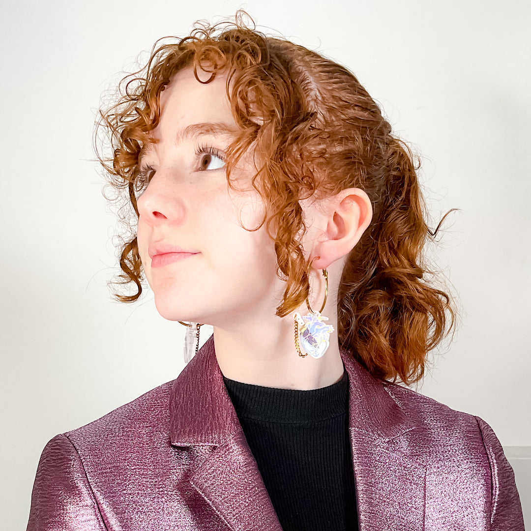 Anatomical heart hoops in iridescent and gold plated stainless steel are shown on a young model for scale.