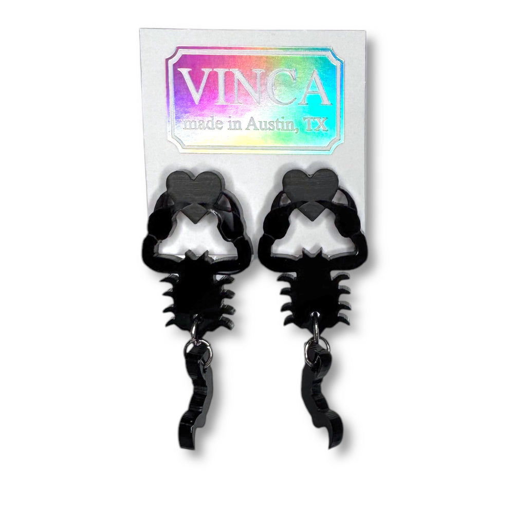 Black scorpion heart earrings on a white card set against a white background. 