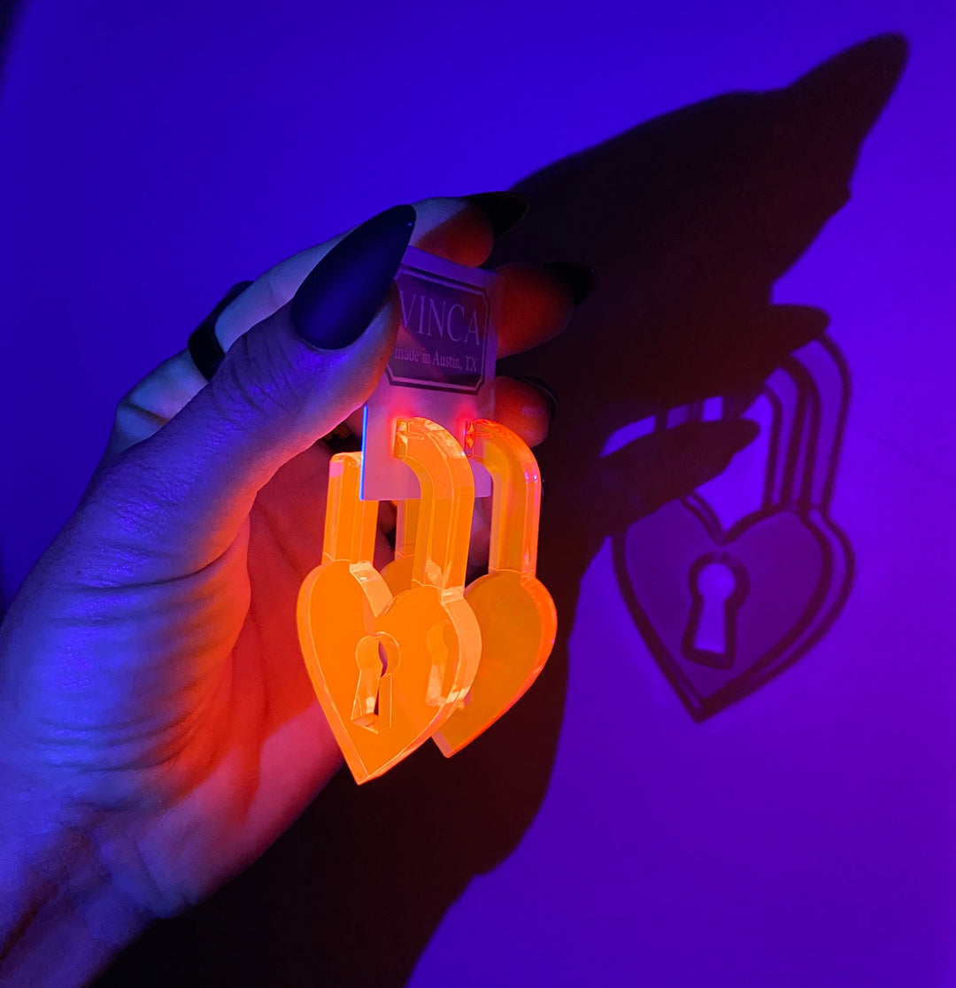 A hand holds two pink heart locks under a blacklight set against a purple background.