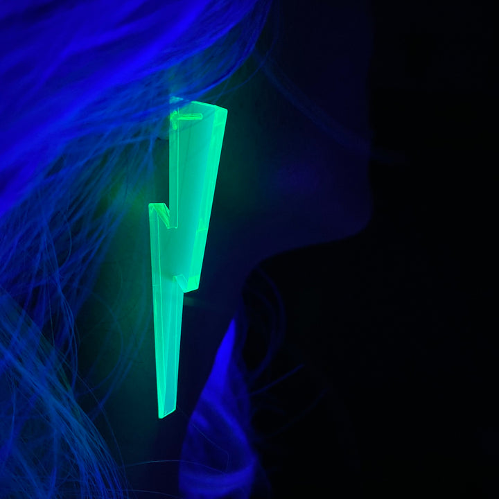 A woman wears a blacklight reactive neon green lightning bolt-shaped earring against a dark background.