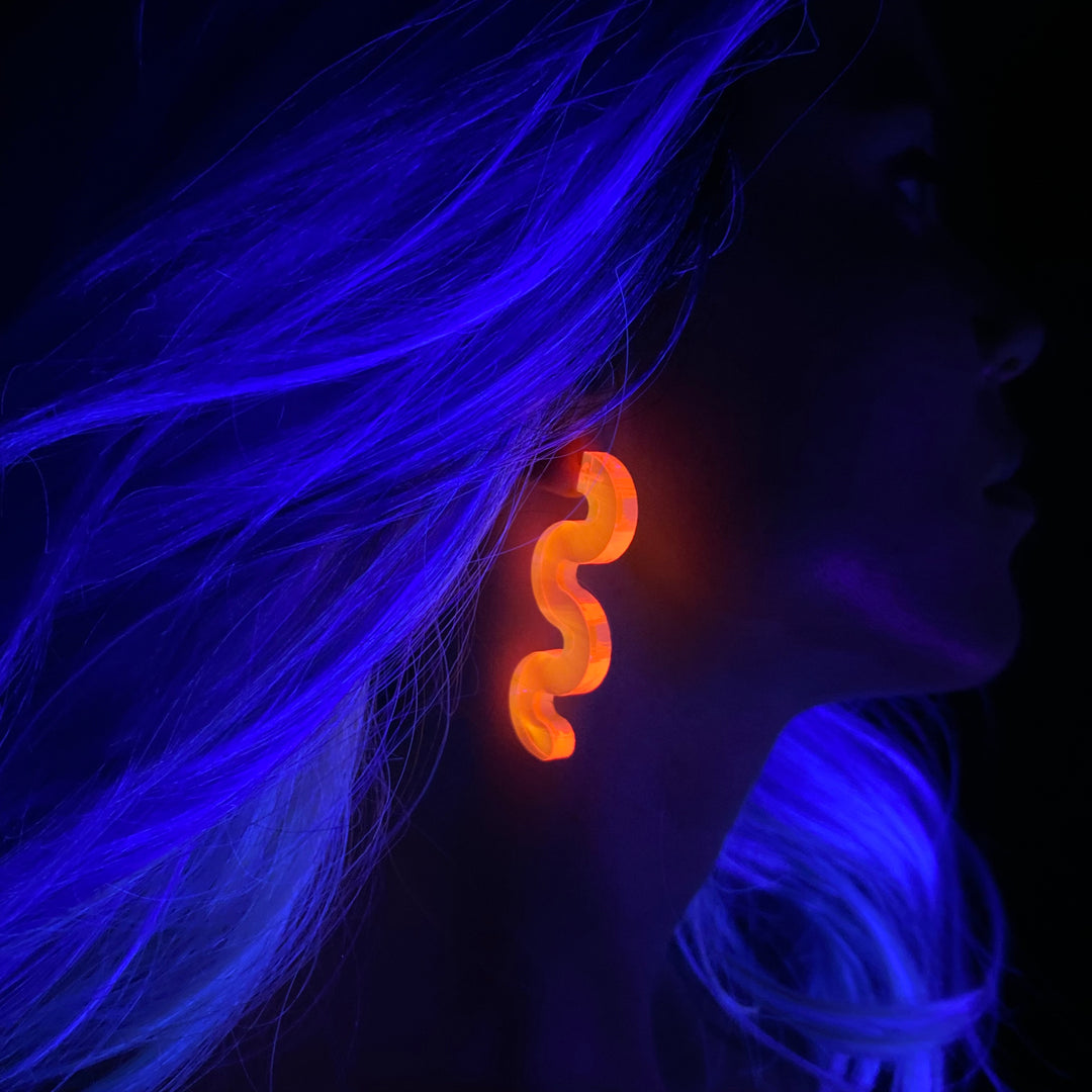 Person with glowing blue hair wearing a glowing pink earring in a dark setting.