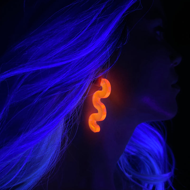 Person with glowing blue hair wearing a glowing pink earring in a dark setting.