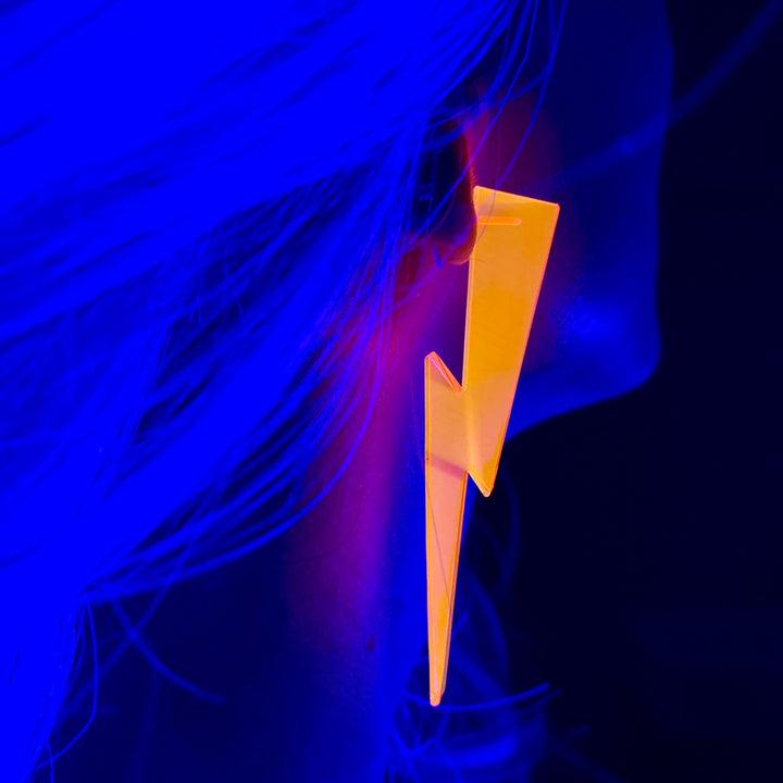 A woman wears a neon pink lightning bolt earring against a blue background.