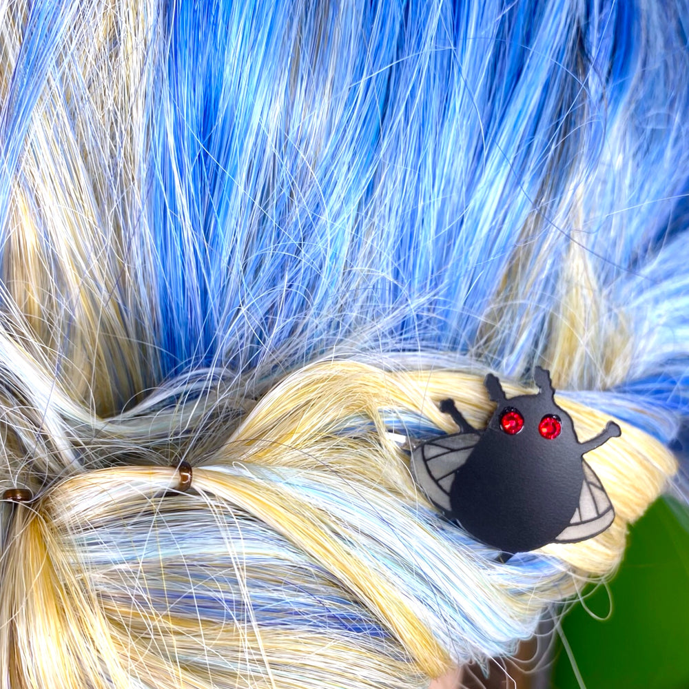 Our Sarah's Scribbles Cryptid Club Moth Man Bobby Pin set sits in a woman's bright blue hair. 