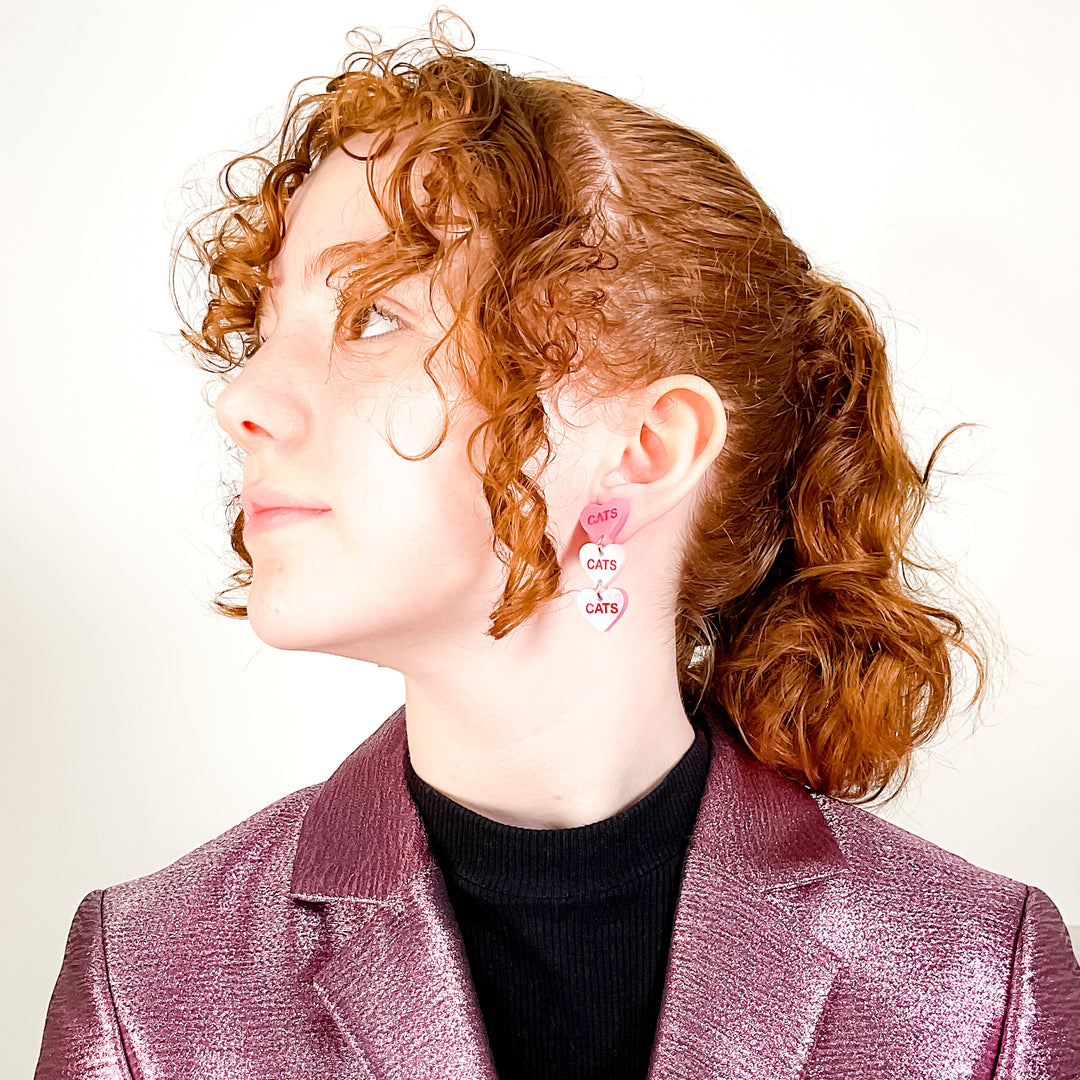 Cat Candy Heart earrings on a young model with curly, red hair and wearing a shimmery pink blazer.