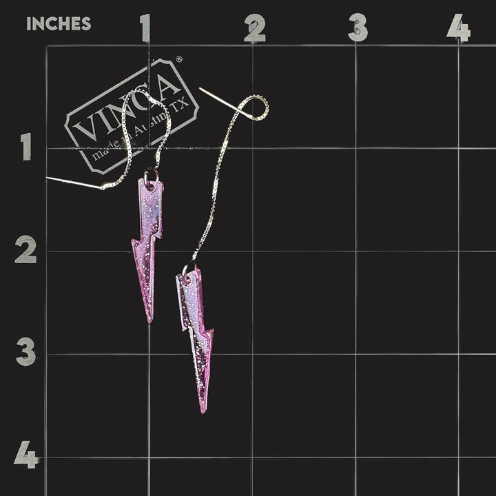 Pink glitter lightning bolt ear threaders on an inch grid mat showing size