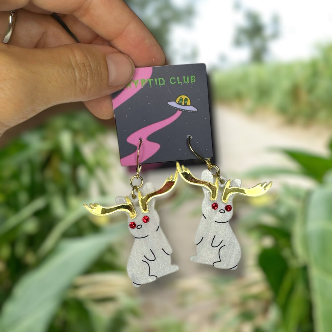 Handmade Sarah's Scribbles Cryptid Club Jackalope rabbit earrings in pearl white with red crystal eyes. We use gold plated stainless steel findings.