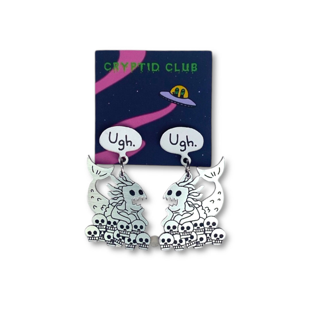 Sarah's Scribbles Cryptid Club Ugh Mermaid Dangle Earrings on a Cryptid Club branded card and set against a white background.