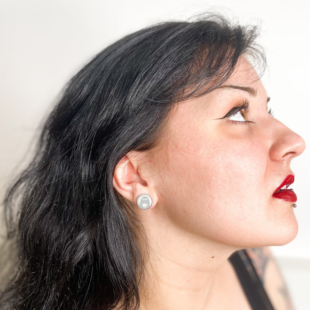 A dark-haired model wears our officially licensed Emily the Strange logo earrings against a white background.