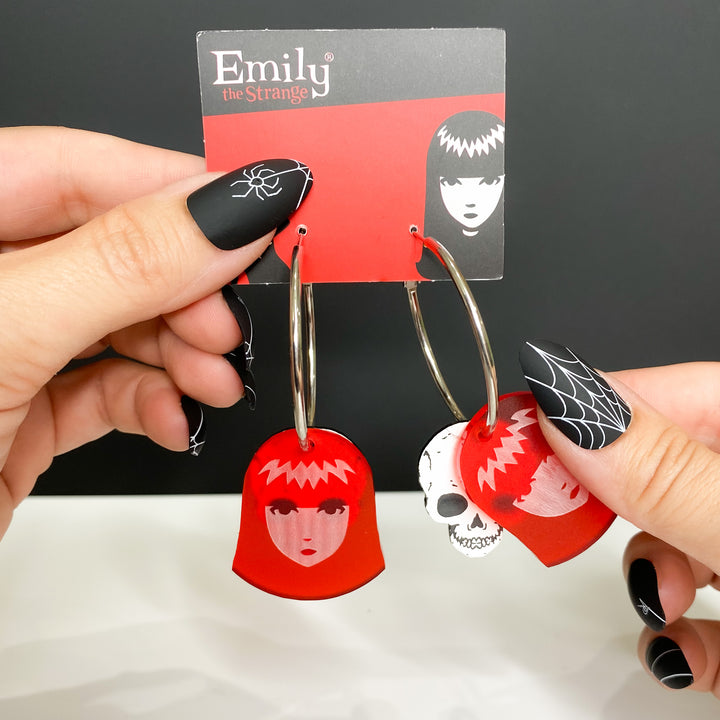 Hands showcase our packaged officially licensed Emily the Strange X-Ray Emily Skull Hoop Earrings set against a white and black background. 