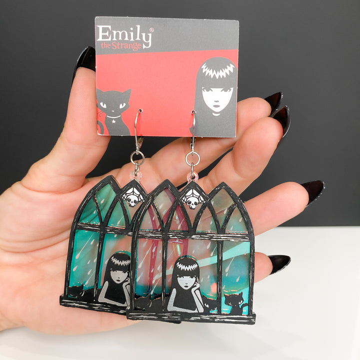 A hand holds our officially licensed Emily the Strange soft goth iridescent window earrings against a white background.