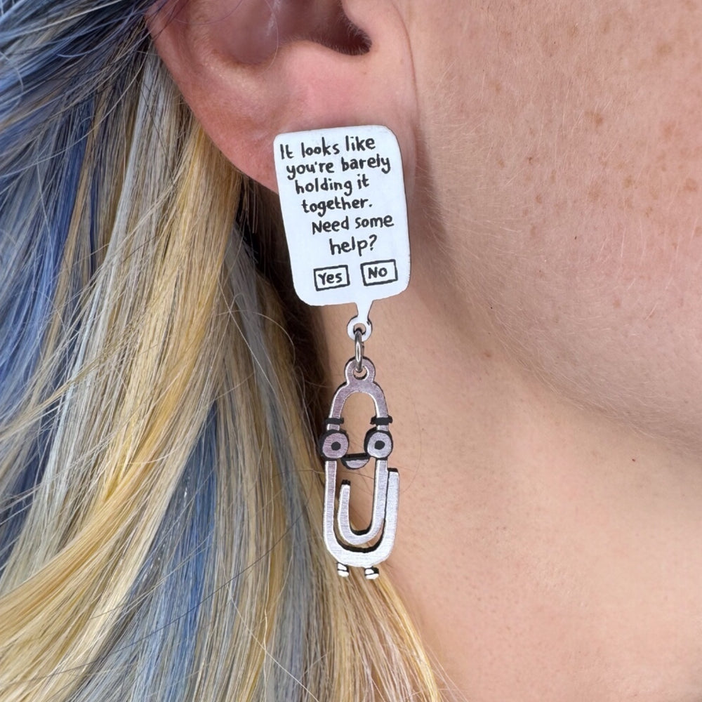 Gemma Correll Clippy the paper clip earring with a humorous message on a person with blue and blonde hair.