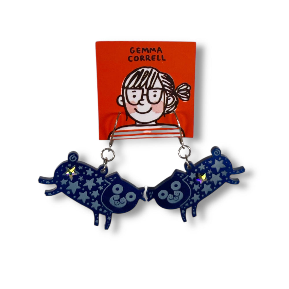Pair of blue pug earrings with star patterns on a white background, featuring a small card with UK illustrator Gemma Correll's branding. 