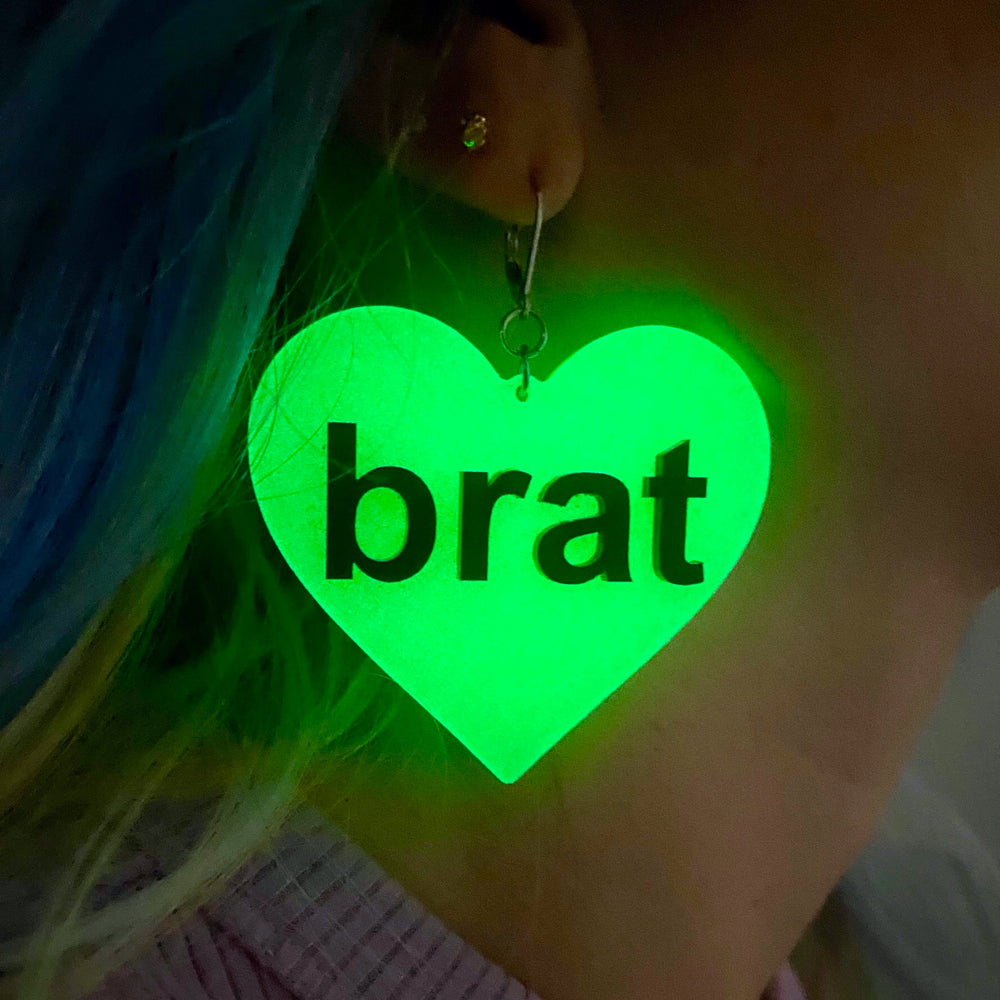 A woman wears a bright green Brat Heart Dangle Earring in the dark.