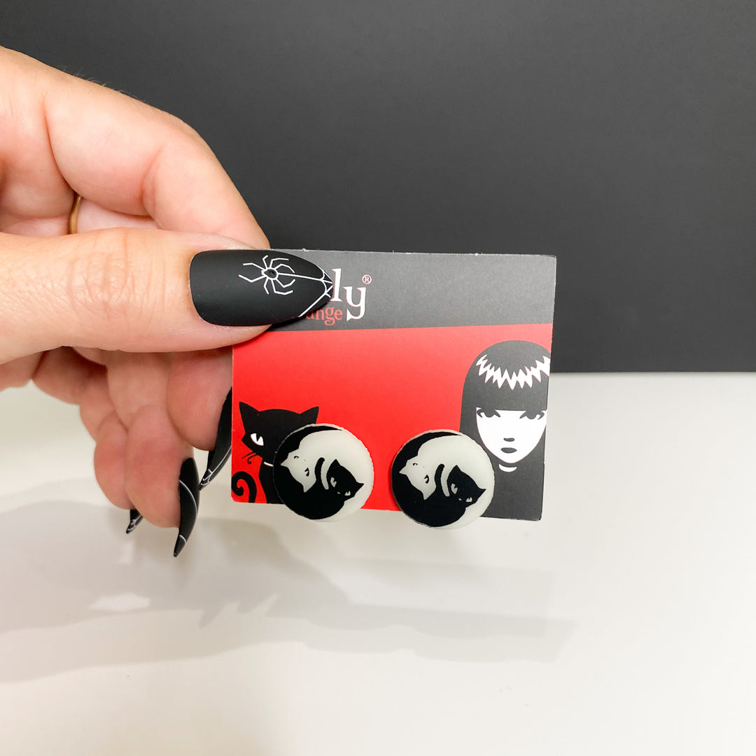 A hand holds our officially licensed Emily the Strange Yin Yang Cat glow-in-the-dark stud earrings on a white background.