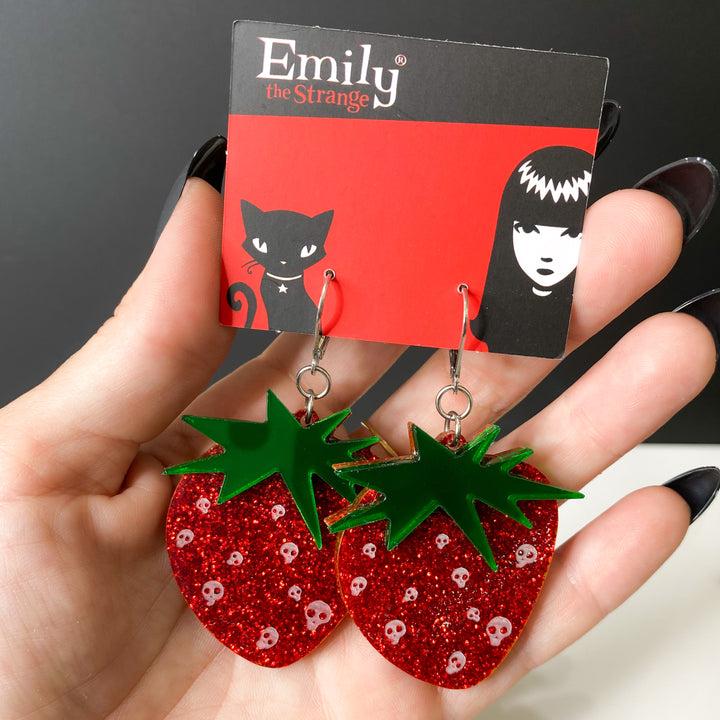 A hand holds our officially licensed Emily the Strange Skullberry strawberry earrings against a white and black background.