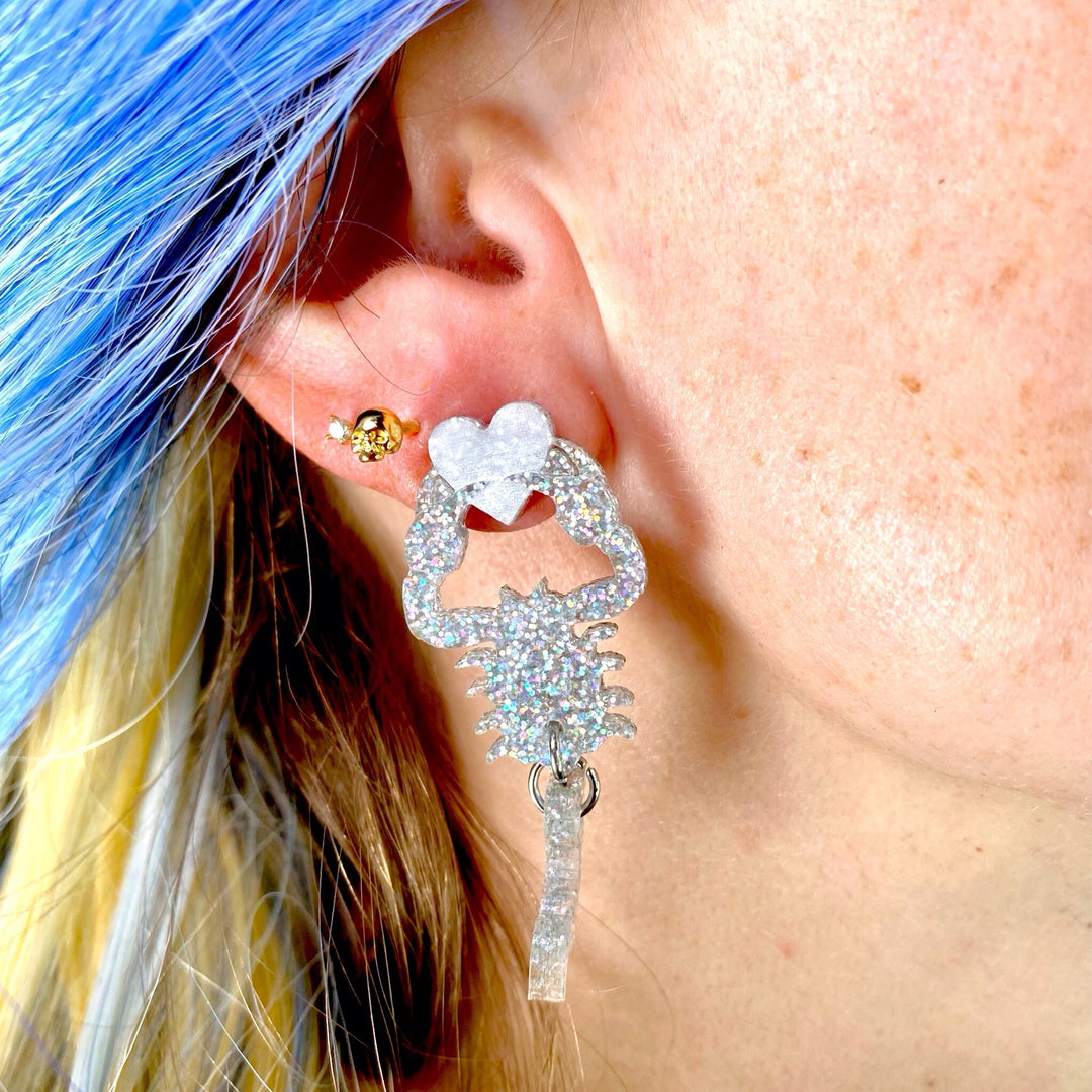 Handmade glitter hologram scorpion earrings worn by a woman with medium length blue ombre hair.