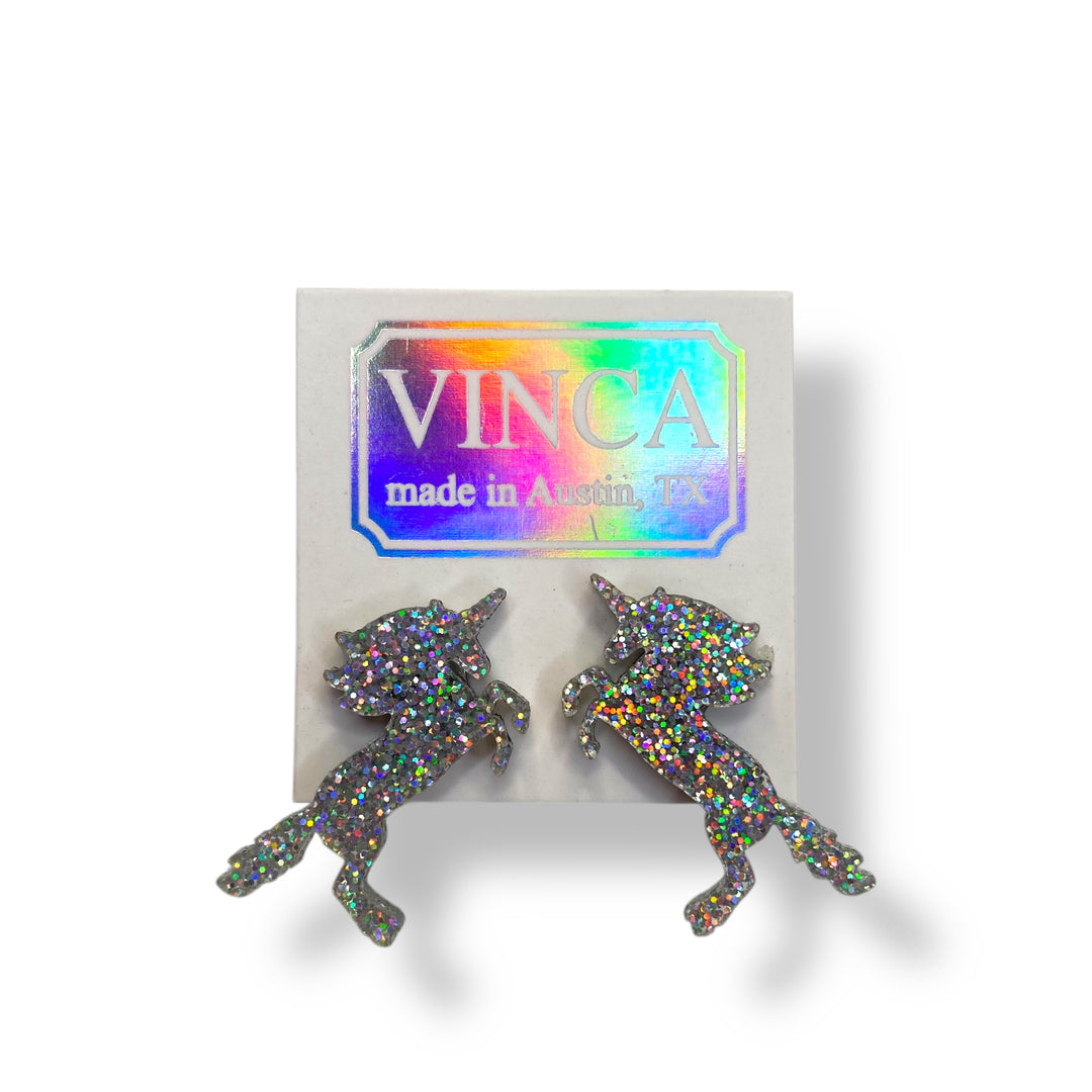 Handmade unicorn earrings in hologram glitter are pierced through a white branded Vinca card and set against a white background. 