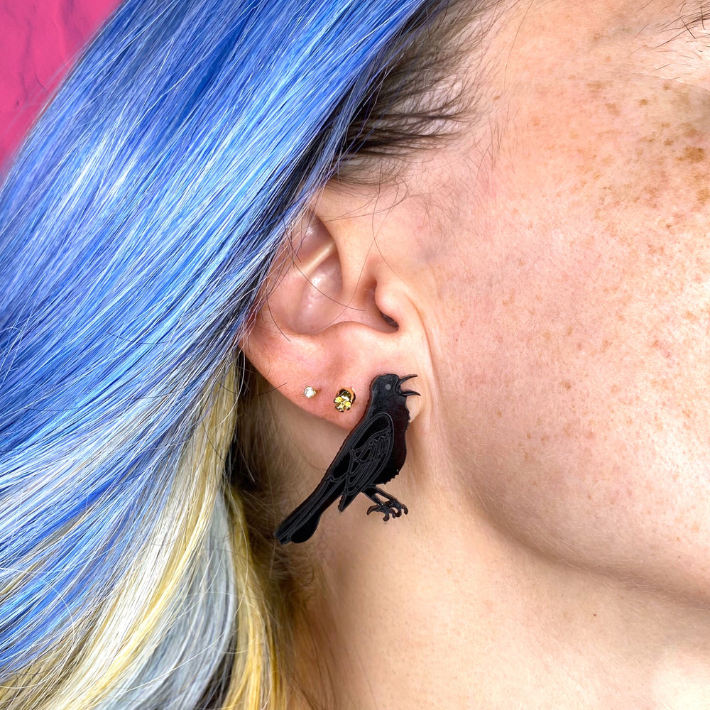 Handmade grackle earrings on a woman with blue hair with light brown roots.