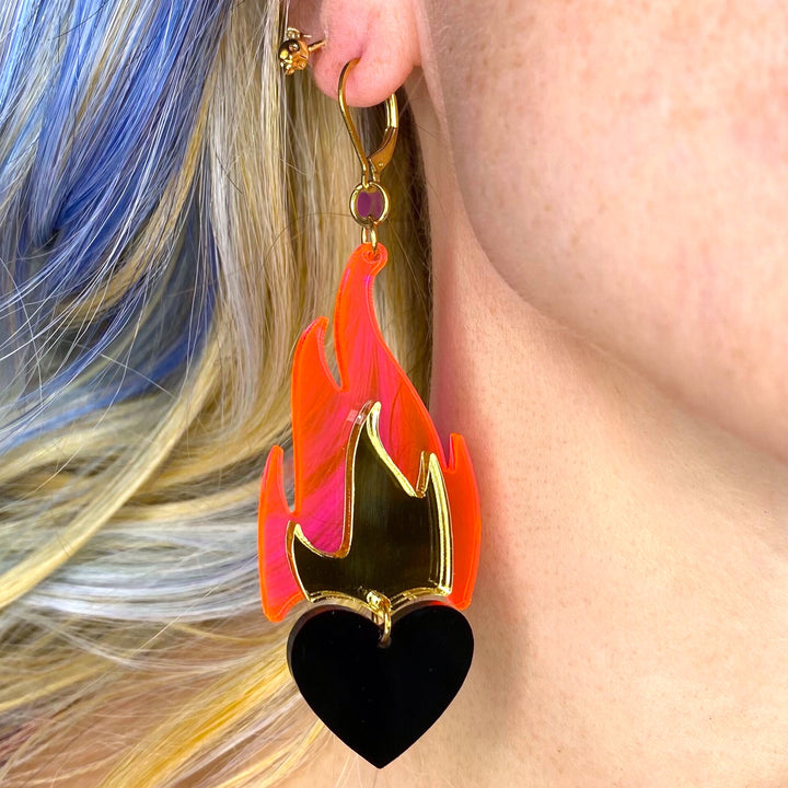 A woman with blue hair wears Vinca's Love A La Flambé earring in transparent neon pink, mirror gold and solid black. 