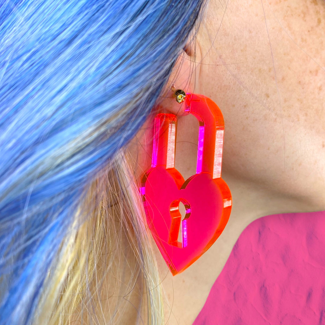 A woman with bright blue hair wears a transparent neon pink Locky in Love earring.