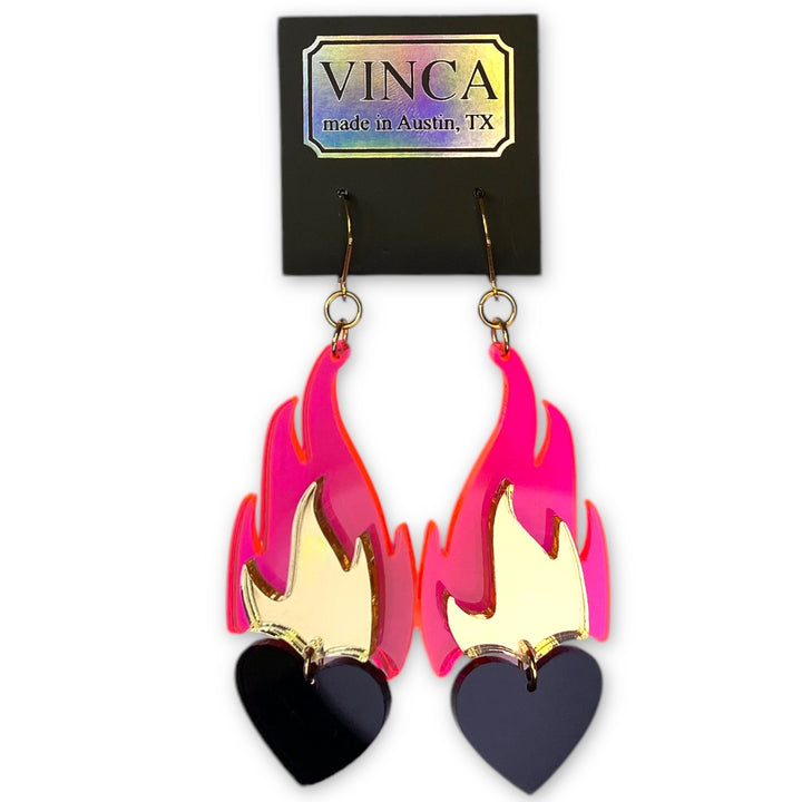 Our Love A La Flambé earrings in transparent neon pink, solid black, mirror gold on a branded black Vinca card floating on a white background.