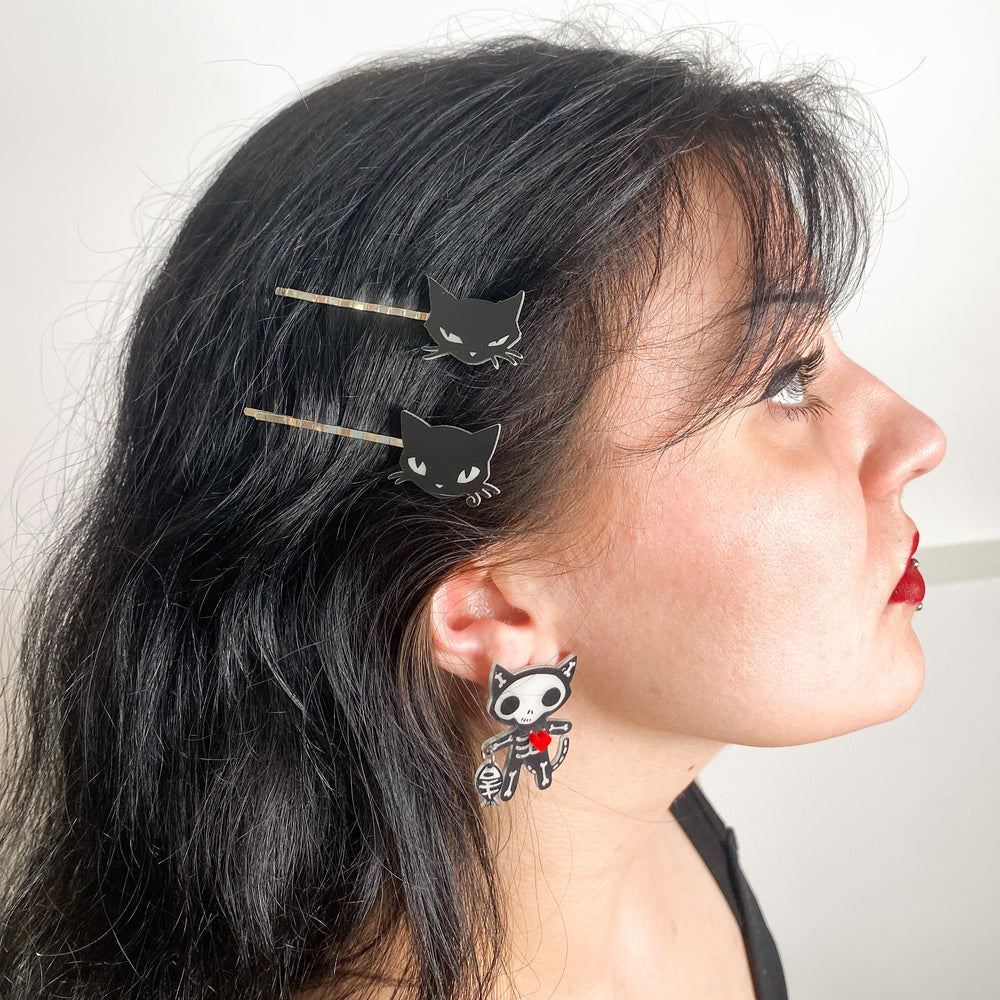 A model wears our officially licensed Emily the Strange goth cat skeleton earrings standing against a white background.