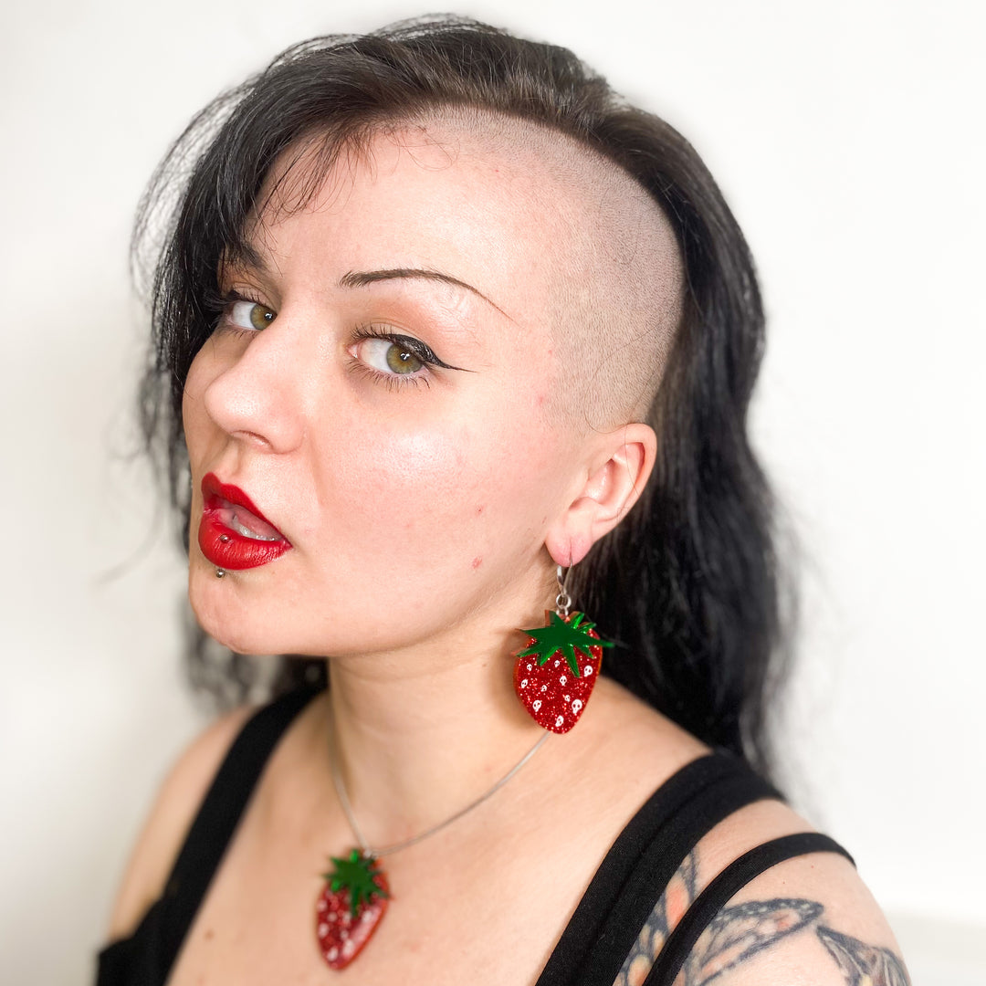 A model wears our officially licensed Emily the Strange Skullberry -strawberry earrings on stainless steel hooks against a white background.