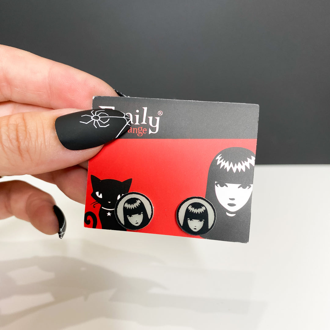 A hand holds a packaged version of our officially licensed Emily the Strange glow-in-the-dark logo earrings against a white and black background.