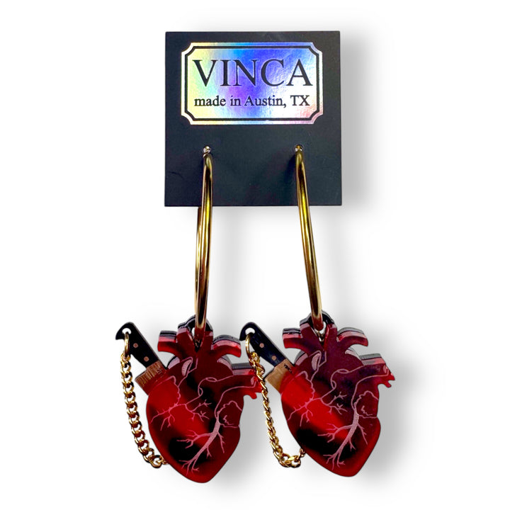 Packaged goth horror anatomical heart hoop earrings in gold plated stainless steel with removable plastic knives.